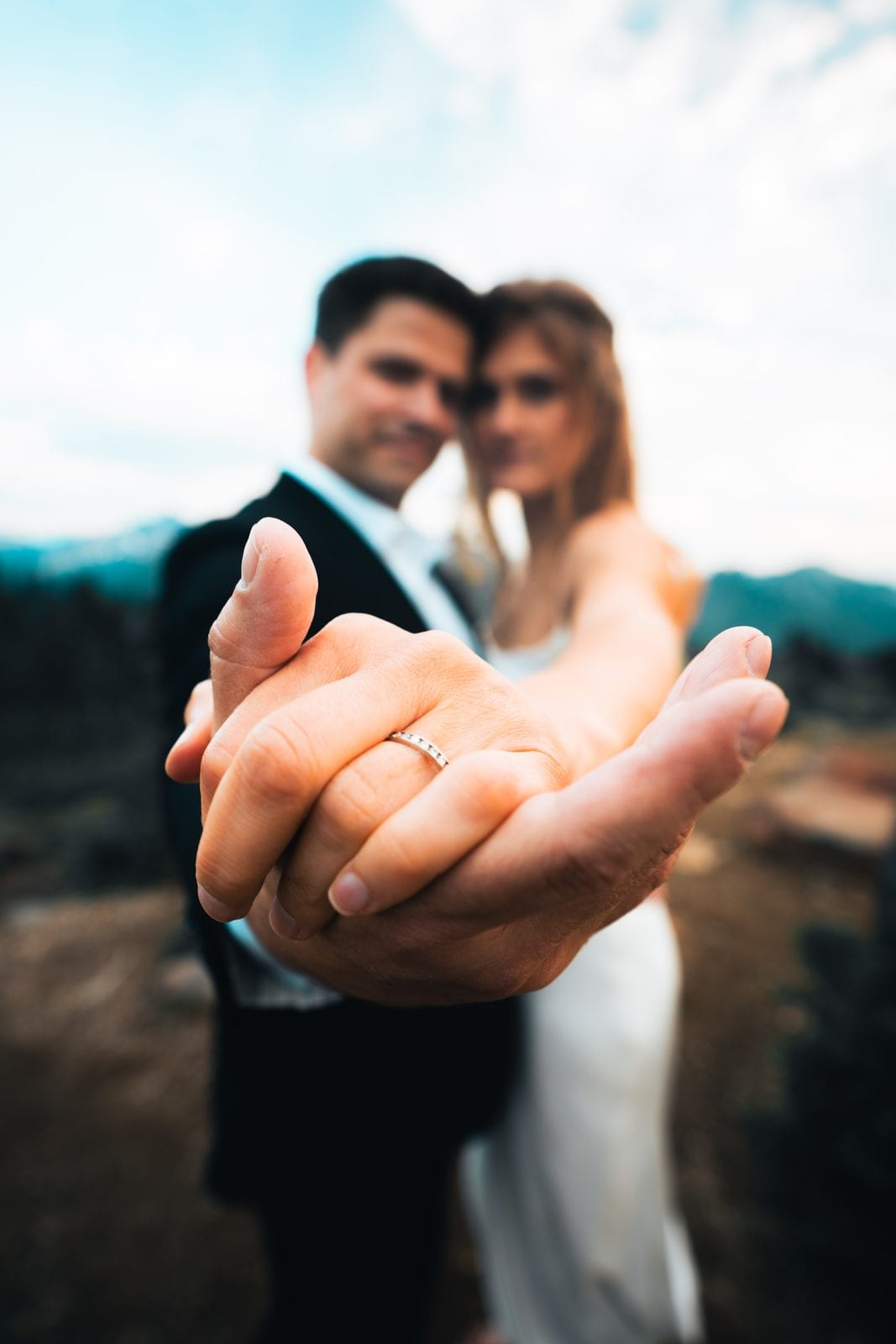 The couple showing their wedding rings, mountains beyond