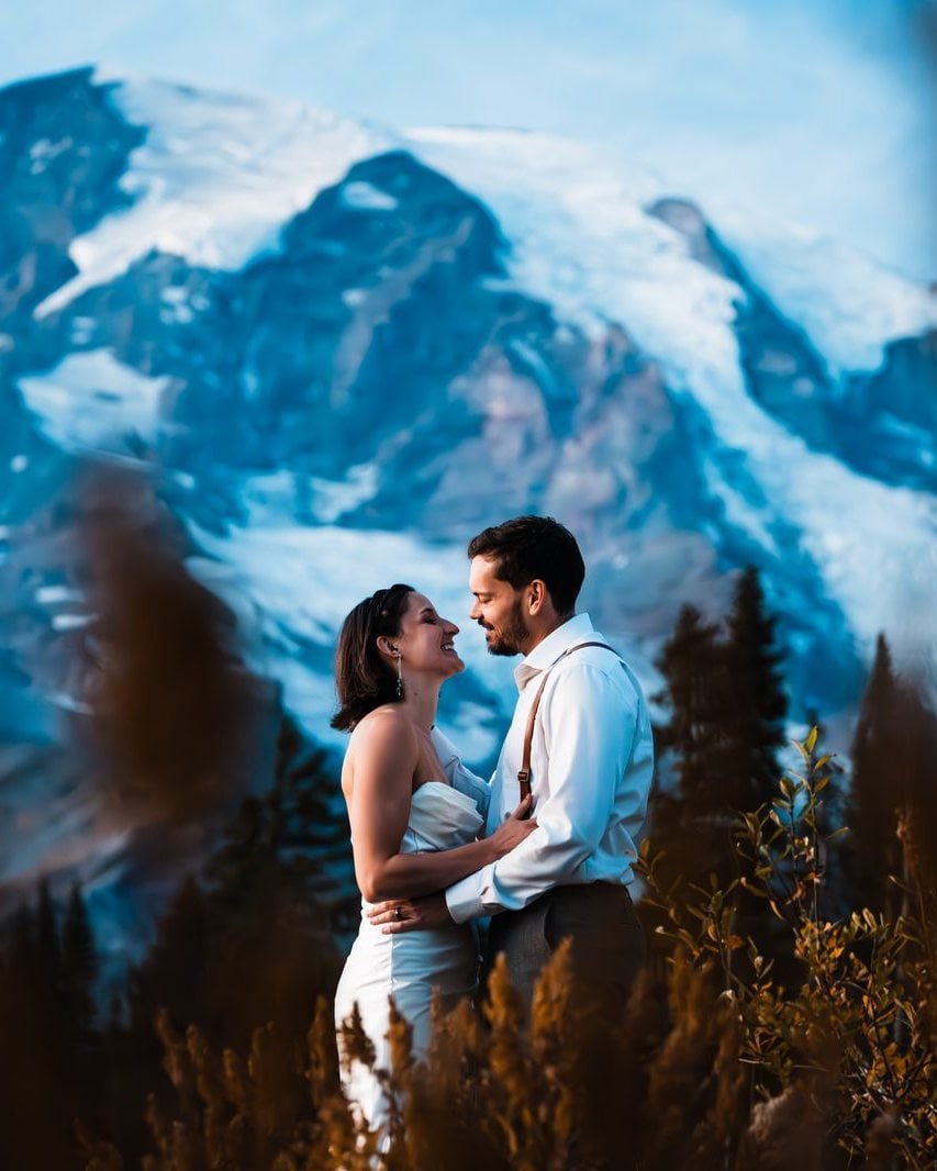 A couple holding each other in a meadow below Mt. Rainier at dusk