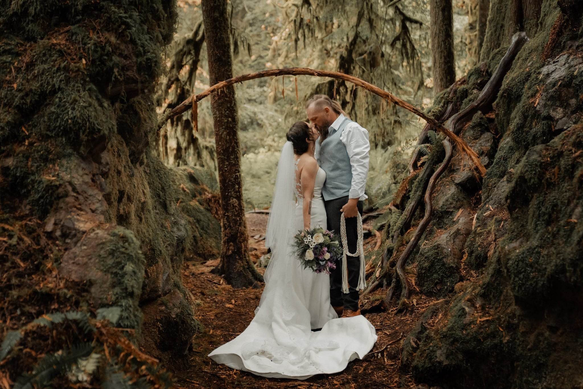 Clay and Amanda under a clear umbrella on a forest footbridge in the rain