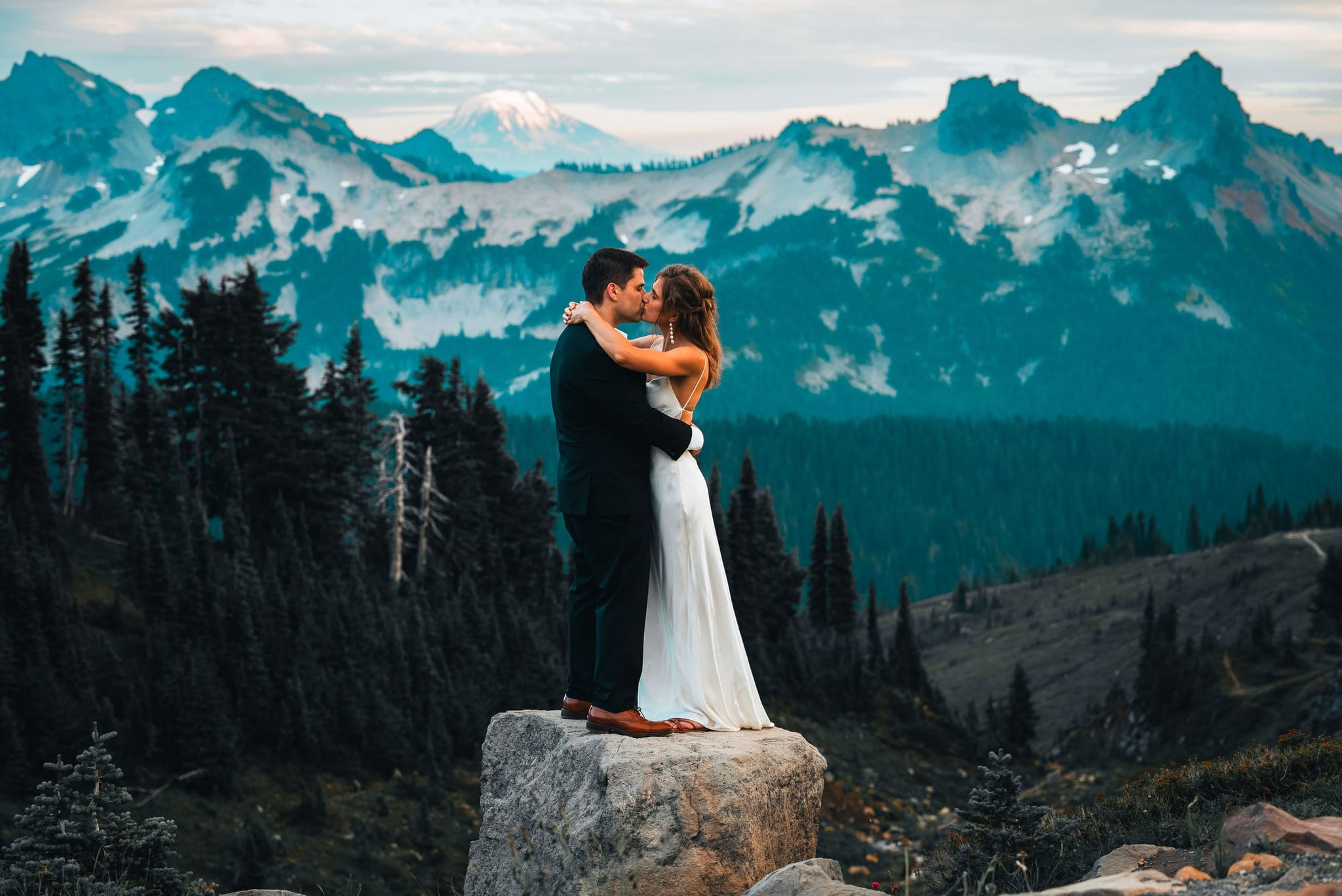 Tyler and Brittany embracing on a rock with a mountain range behind them